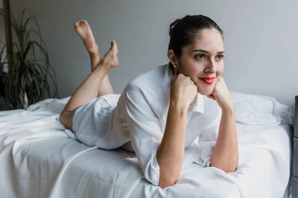 Portrait of mature latin woman relaxing down on bed laughing at home in Mexico Latin America, hispanic female