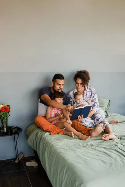 young latin family with children reading a book together on bed at home in Mexico, Hispanic mother, father, daughter and baby in Latin America