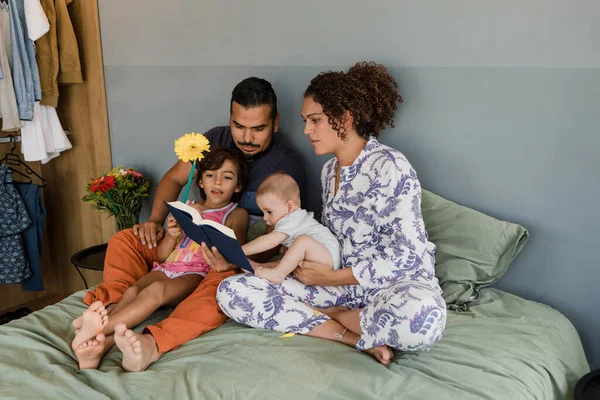 young latin family with children reading a book together on bed at home in Mexico, Hispanic mother, father, daughter and baby in Latin America