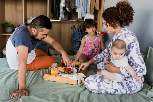 latin family having breakfast on bed at home in Mexico, hispanic mother, father, daughter and son at morning in Latin America