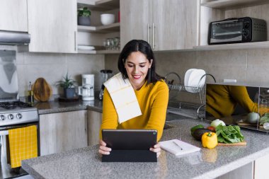 Latin yetişkin kadın sağlıklı yemek pişiriyor ve elinde dijital tablet tutuyor Meksika mutfağında Meksika Latin Amerika 'da bir yemek tarifi okuyor, İspanyol kadın.