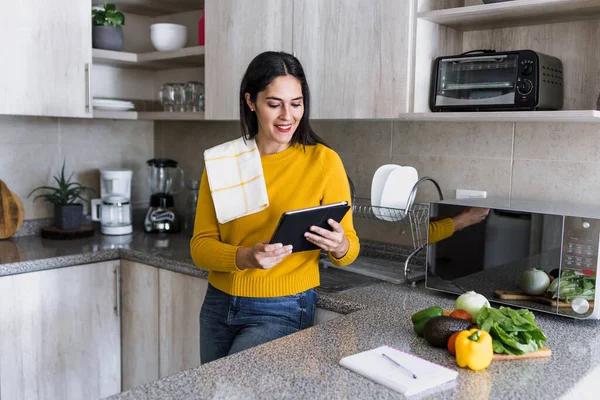 Latin yetişkin kadın sağlıklı yemek pişiriyor ve elinde dijital tablet tutuyor Meksika mutfağında Meksika Latin Amerika 'da bir yemek tarifi okuyor, İspanyol kadın.