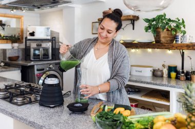 Latin Amerika 'da çatı katında yeşil meyve suyu içen Latin bir kadın, evde Meksikalı bir kadın.