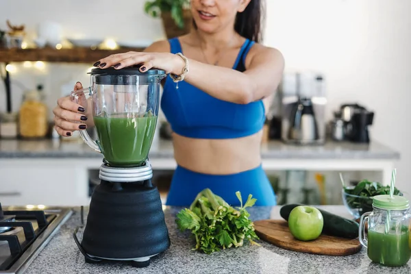 Latin woman pouring green juice from mixer into glass in kitchen at home in Mexico Latin America, hispanic female on detox diet