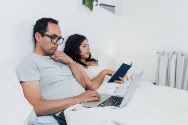 Latin çift kitap okuyor ve Meksika 'daki evlerinde dizüstü bilgisayar kullanıyor. Latin Amerika' da Latin insanlar dinleniyor.