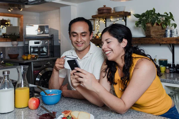 latin couple having breakfast and using mobile phone at kitchen in home in Mexico Latin America, hispanic people having fun