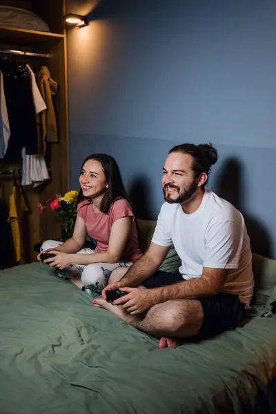 young latin couple of gamers playing video games on bed at night in home in Mexico Latin America, hispanic people having fun