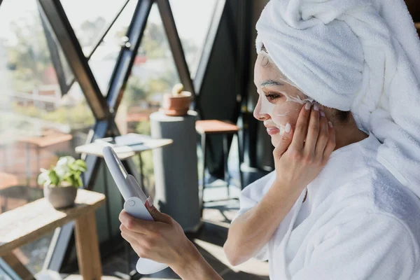 young latin woman with facial mask on her face for Skin care looking a mirror at home in Mexico Latin America, hispanic female health care