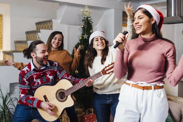 Latin friends singing in karaoke party celebrating christmas at home in Mexico Latin America