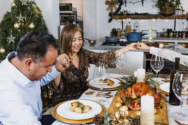 Latin Family praying and holding hands at Christmas dinner at home in Mexico. Grateful people with gratitude enjoy a turkey meal in Latin America, teenagers son, daughter, mother and father