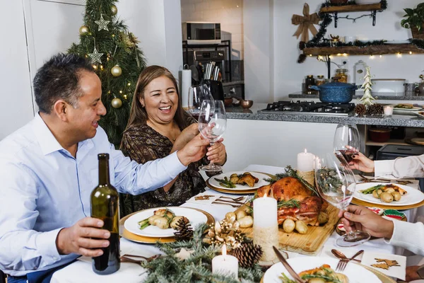 Latin family having Christmas dinner and making wine toast at home in Mexico Latin America, hispanic teenagers daughter, son, mother and father