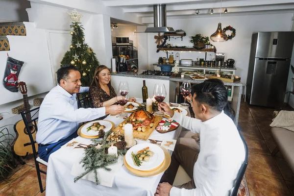 Latin family having Christmas dinner and making wine toast at home in Mexico Latin America, hispanic teenagers daughter, son, mother and father