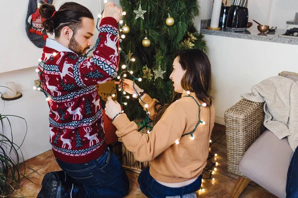 Latin couple placing Christmas lights on Christmas tree at home in Mexico Latin America, woman and man in holidays