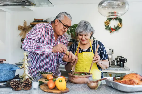 Latin senior couple cooking a turkey meat together for Christmas dinner at home in Mexico Latin America, hispanic middle aged people preparing food in holidays
