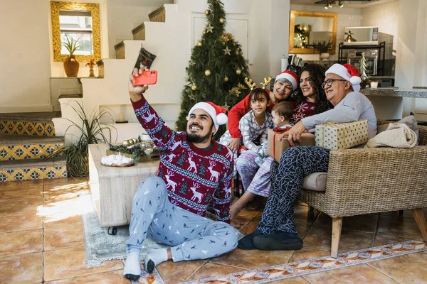 Latin family taking selfie portrait with mobile phone during Christmas at home in Mexico Latin America. hispanic people grandparents daughter, mother and father with santa hat