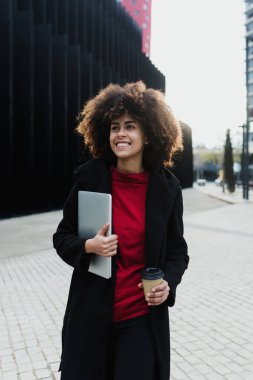 Latin Amerika 'da dizüstü bilgisayar kullanan genç Afrikalı Amerikalı iş kadını, afro saçlı ve gökdelen geçmişi olan İspanyol ve Karayipliler.