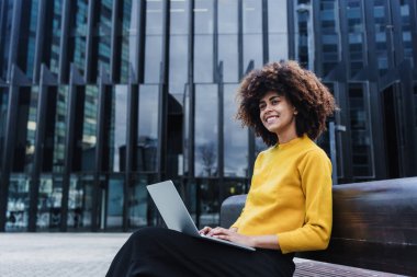 Latin Amerika 'da dizüstü bilgisayar kullanan genç Afrikalı Amerikalı iş kadını, afro saçlı ve gökdelen geçmişi olan İspanyol ve Karayipliler.