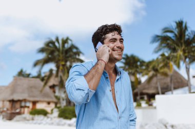 Tatillerde veya tatillerde Meksika 'da Latin Amerika, Karayipler ve tropikal bölgelerde telefonla konuşan İspanyol bir adam.