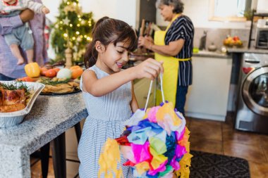 Mexican child girl holding a mexican pinata at home in Mexico celebrating traditional posadas for Christmas in Latin America clipart