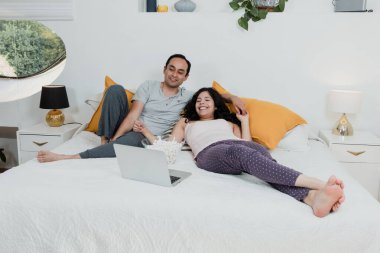 Latin Amerikalı genç bir çift dizüstü bilgisayar ya da dizüstü bilgisayarla film izliyor. Latin Amerika 'daki evlerinde yatıyorlar. Latin kökenli insanlar yatak odasında patlamış mısır yiyorlar.