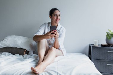 Yetişkin Latin kadın portresi. Telefon kullanıyor ve yatakta dinleniyor. Meksika 'da Latin Amerika' da evde gülüyor.