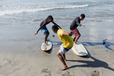 Latin sörf eğitmeni ve iki erkek sörfçü Acapulco Mexico 'daki plajda sörf dersinde sörf tahtasında durmaya çalışıyorlar. Latin Amerika' da yaz sporlarında sörf yapan İspanyol insanlar.