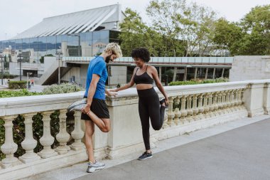 İspanya 'da bir şehir parkında spor giysileri giyerek antrenmandan önce esneme hareketleri yapan çok ırklı iki arkadaş. İspanyol adam ve afro saçlı kadın birlikte egzersiz yapıyorlar. 