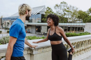 İspanya 'da bir şehir parkında spor giysileri giyerek antrenmandan önce esneme hareketleri yapan çok ırklı iki arkadaş. İspanyol adam ve afro saçlı kadın birlikte egzersiz yapıyorlar. 