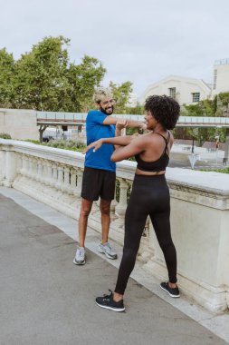 İspanya 'da bir şehir parkında spor giysileri giyerek antrenmandan önce esneme hareketleri yapan çok ırklı iki arkadaş. İspanyol adam ve afro saçlı kadın birlikte egzersiz yapıyorlar. 