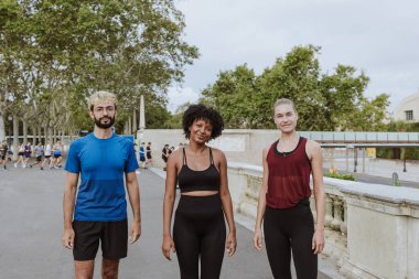 İspanya 'da bir şehir parkında birlikte egzersiz yaptıktan sonra su ya da kahve içen ve dinlenen bir grup arkadaş. İspanyol adam ve afro saçlı kadın atletik kıyafetler giyiyorlar.