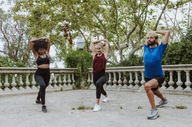 İspanya 'da bir şehir parkında spor kıyafetleri içinde antrenman yapmadan önce esneme hareketleri yapan çok ırklı bir arkadaş grubu. İspanyol adam ve afro saçlı kadın birlikte egzersiz yapıyorlar. 