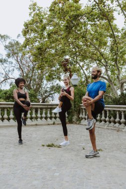 İspanya 'da bir şehir parkında spor kıyafetleri içinde antrenman yapmadan önce esneme hareketleri yapan çok ırklı bir arkadaş grubu. İspanyol adam ve afro saçlı kadın birlikte egzersiz yapıyorlar. 
