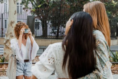 İspanyol ve çok ırklı kızlar şehrin caddesinde klasik kamerayla fotoğraf çekiyorlar. Bir grup çok ırklı kadın arkadaş.