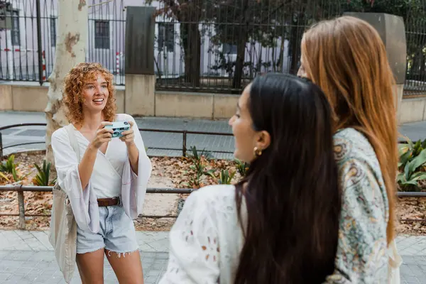 İspanyol ve çok ırklı kızlar şehrin caddesinde klasik kamerayla fotoğraf çekiyorlar. Bir grup çok ırklı kadın arkadaş.