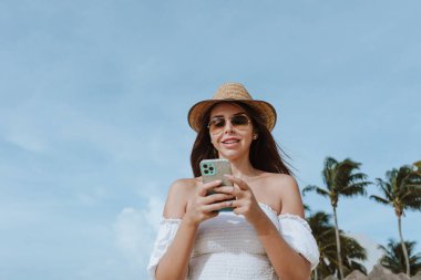 Latin Amerika, Karayipler ve tropikal bölgelerde tatillerde veya tatillerde cep telefonu kullanan İspanyol genç kadın.