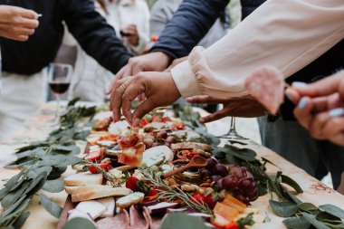 Eller ve açık büfe tahtası, ahşap masada şarap ve peynir.