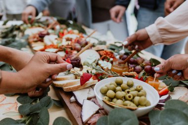 Eller ve açık büfe tahtası, ahşap masada şarap ve peynir.