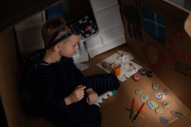 Ukraynalı bir çocuk karton bir evde ışıksız oturuyor ve resim çiziyor. Nazilerin bombardımanından sonra Ukraynalı bir çocuk karanlık bir odada fenerle resim çiziyor. Ukrayna 'da Savaş