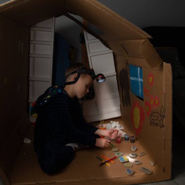 Ukraynalı bir çocuk karton bir evde ışıksız oturuyor ve resim çiziyor. Nazilerin bombardımanından sonra Ukraynalı bir çocuk karanlık bir odada fenerle resim çiziyor. Ukrayna 'da Savaş