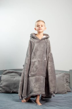 A six-year-old boy of European appearance is dressed in gray pajamas, jumping and having fun on a gray bed.