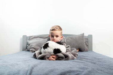 A six-year-old boy plays with a stuffed toy in the form of a soccer ball on the bed.hugs the ball