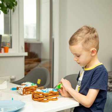 A six-year-old boy of European appearance decorates gingerbread with cream. Cooking in the kitchen