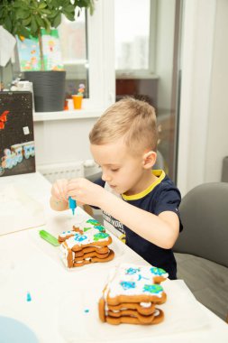 A six-year-old boy of European appearance decorates gingerbread with cream. Cooking in the kitchen