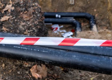 Topraktaki siyah borular ve kum. Şehirdeki kanalizasyon borularının kurulumu. Kapat.