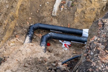 Topraktaki siyah borular ve kum. Şehirdeki kanalizasyon borularının kurulumu. Kapat.