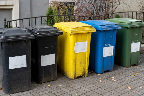 Black, blue, yellow, green garbage recycling bins on street in city. Separate waste, preserve the environment concept. Segregate waste, sorting garbage. Colored trash cans with paper, glass, plastic