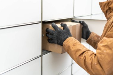 Posta terminalinin yanında elinde kutu olan bir adam. Paket teslimat makinesi. Elinde bir karton kutu tutan kişi. Posta ve posta servisi, online alışveriş, e-ticaret konsepti