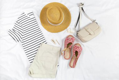 White t shirt, shorts, straw hat, sandals, bag on white background. Top view of woman's spring casual outfit. Simple basic summer women clothes. Flat lay.