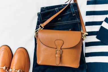 Blue jeans, t shirt, bag and white sneakers on white bed. Trendy clothes. Women's casual spring summer outfit. Fashion concept. Flat lay, top view