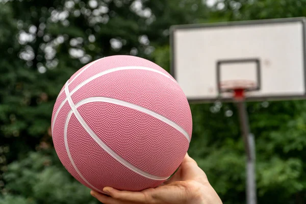Pink basketball ball in man's hands in front of a basket outdoors. Minimal sport background. Sports gear, close up